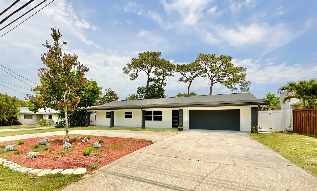 White house with a gray garage door, red mulch landscaping, and driveway under a blue sky.