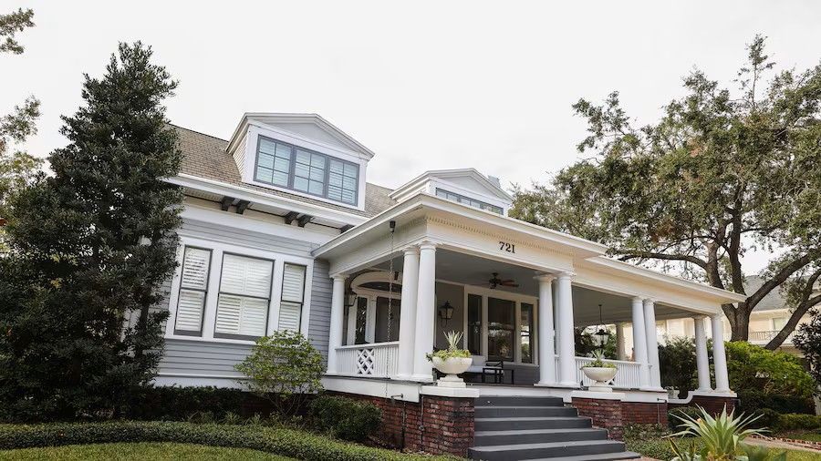 Light blue two-story house with white trim, porch, and dormers under a cloudy sky.