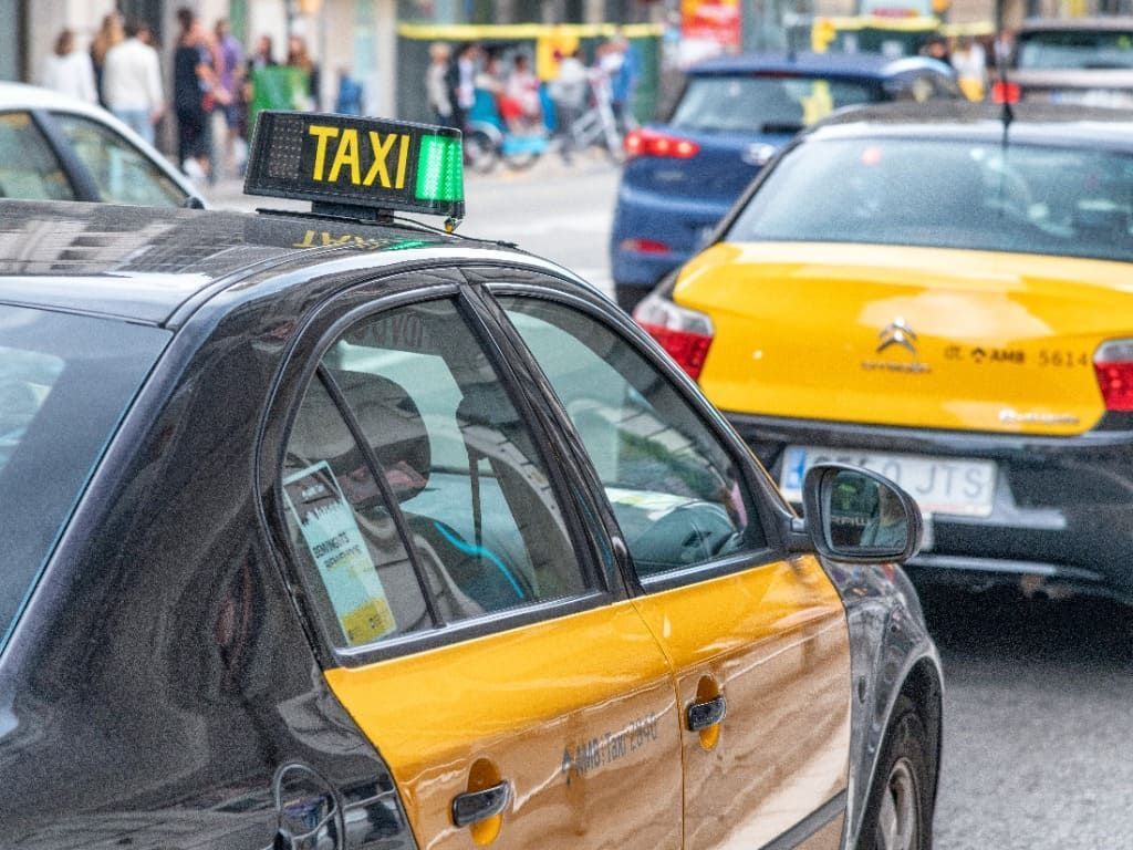 Tres taxis circulan por una calle frente a un gran edificio.