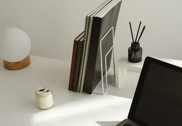 Hay una computadora portátil sobre un escritorio al lado de un soporte para libros y una vela.