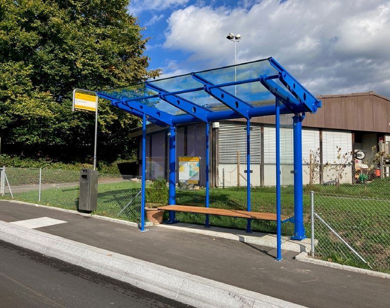 Blaue Bushaltestelle mit Bank und Schild auf einem Gehweg neben einer Straße.
