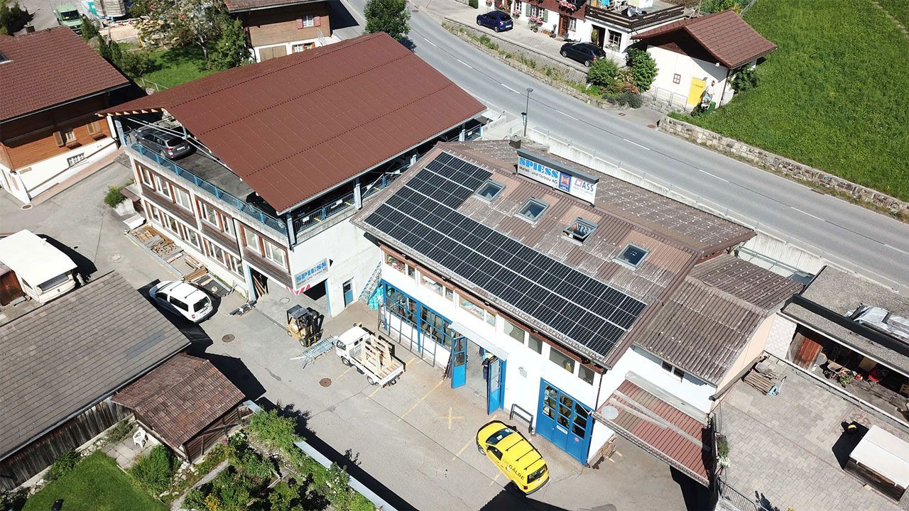 Luftaufnahme eines Gebäudekomplexes mit braunen Dächern, Solarpaneelen und einem gepflasterten Innenhof.