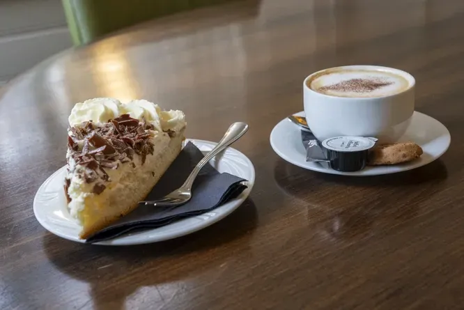 A slice of cake and a cup of coffee on a wooden table.