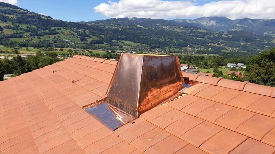 Cheminée en cuivre sur un toit de tuiles rouges, avec une montagne en arrière-plan.