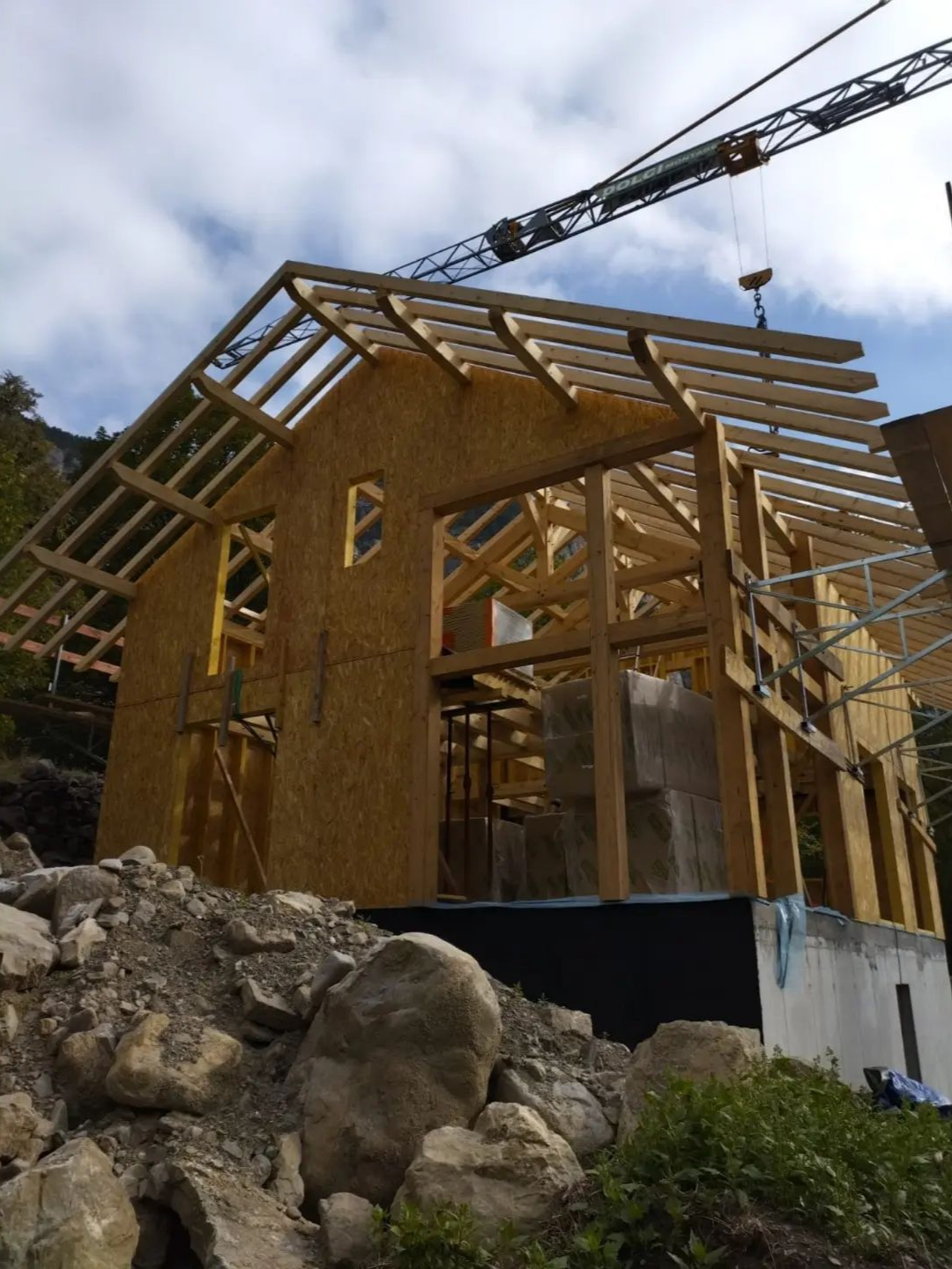 Maison en bois en construction avec une charpente apparente et une grue au-dessus.