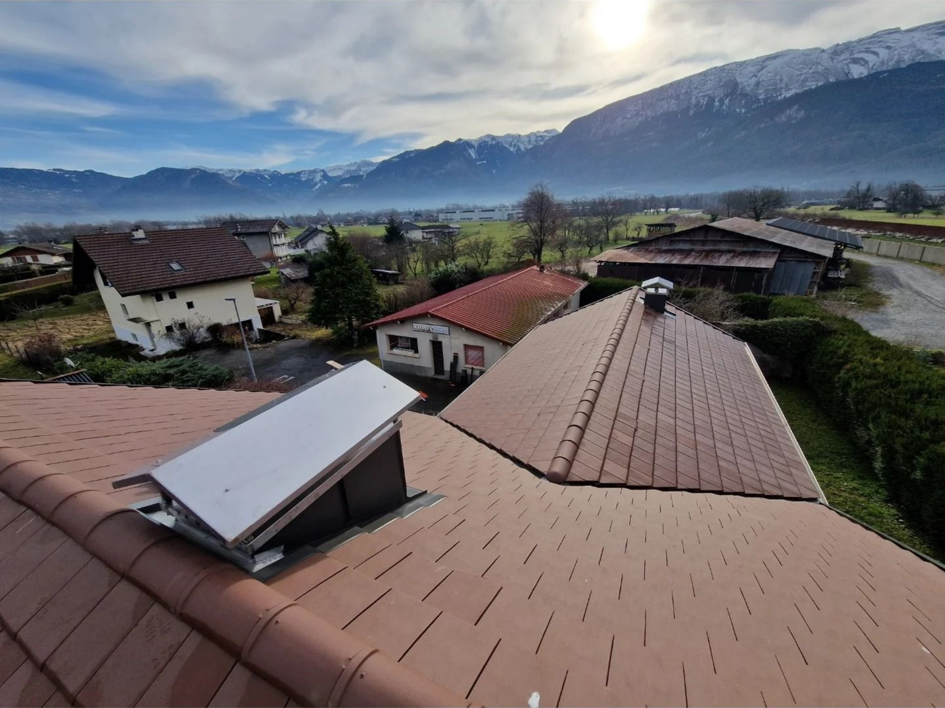 Rénovation de la toiture avec des tuiles rouges, montagnes enneigées en arrière-plan.