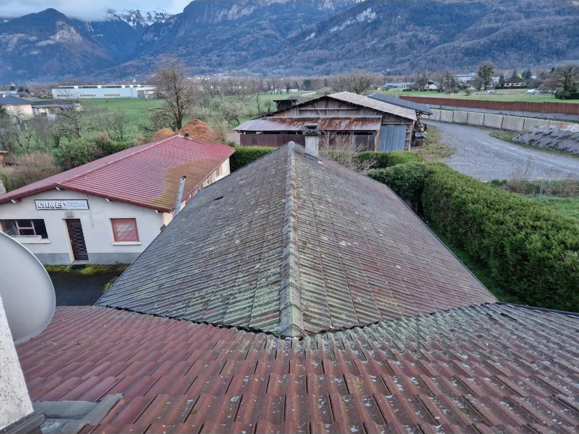 Toit avec tuiles usées sur une maison avec montagnes en arrière-plan.