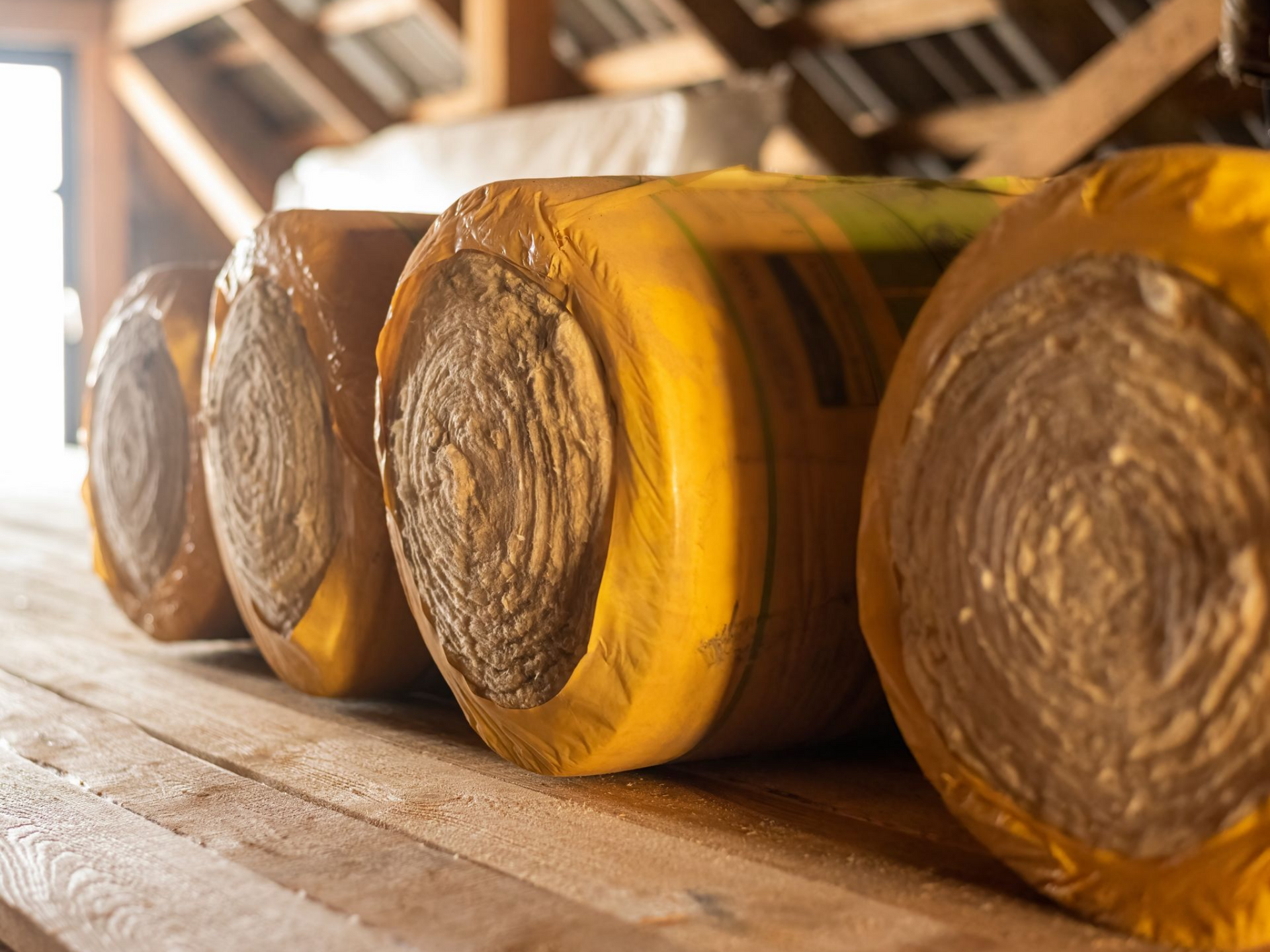 Des rouleaux de laine de verre enveloppés dans du plastique jaune posés sur un plancher.