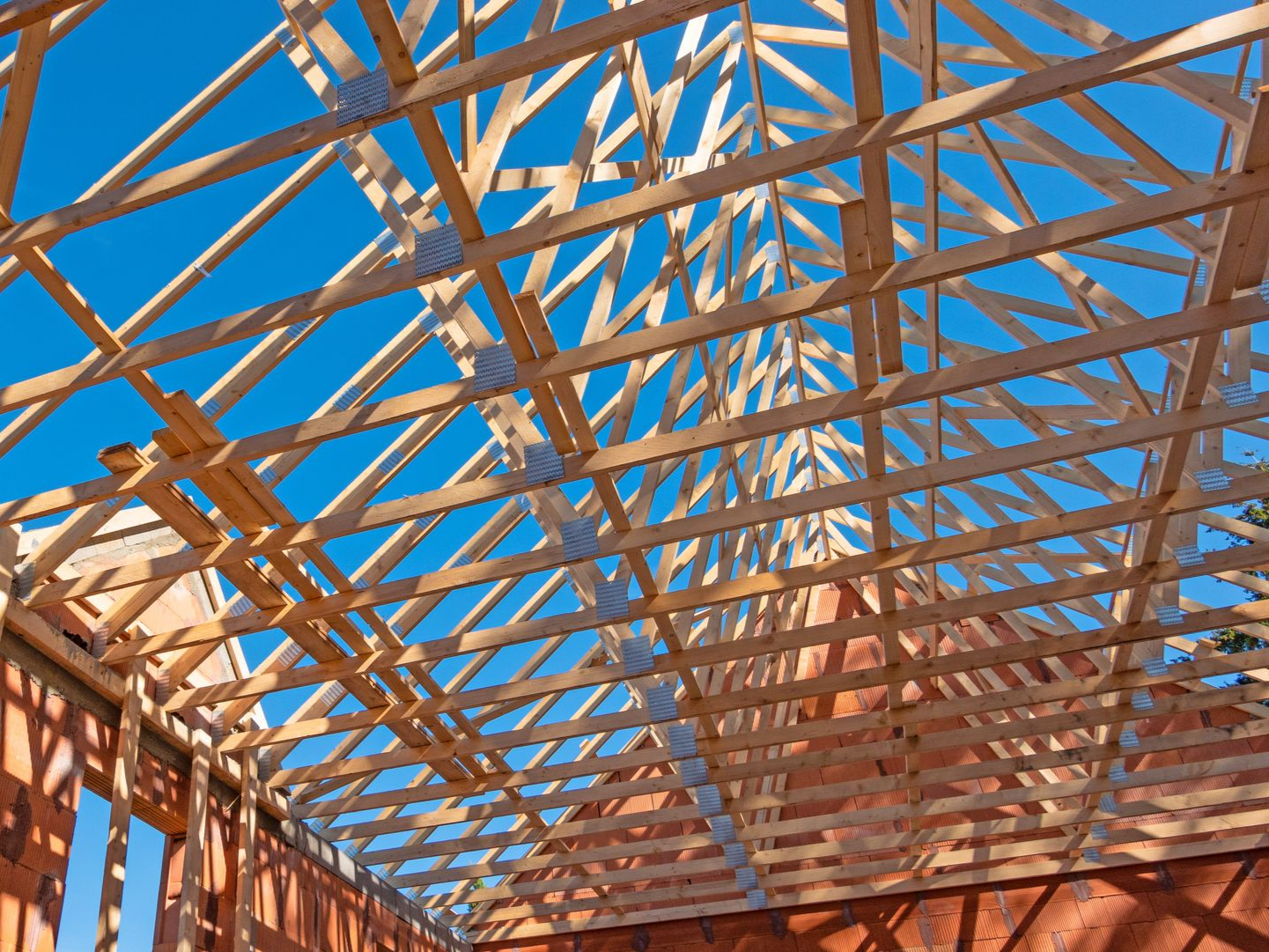 Charpente de toit en bois en construction, sur fond de ciel bleu.