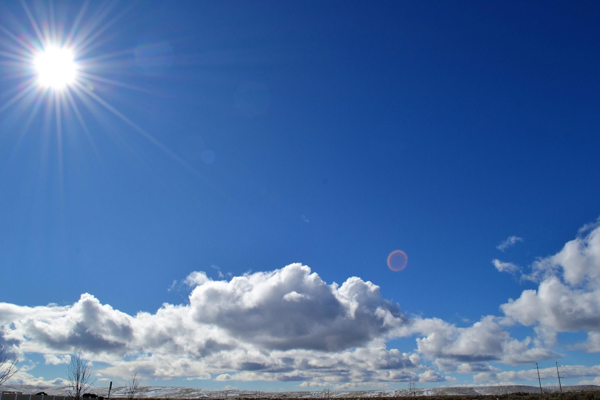 Strahlende Sonne scheint an einem blauen Himmel mit flauschigen weißen Wolken.