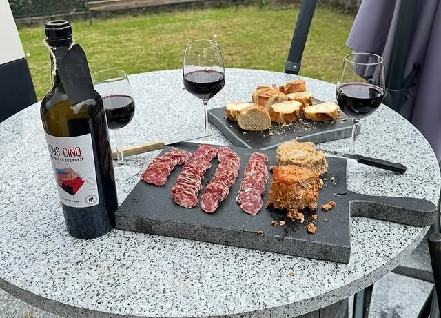 Planche de charcuterie avec vin rouge sur une table d'extérieur. Saucisse et pain en tranches sont disposés sur une planche en pierre grise.