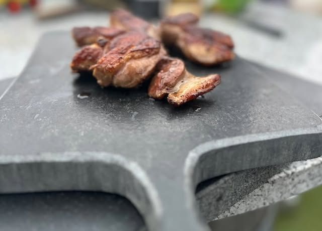 Viande grillée sur une spatule en granit noir à l'extérieur.