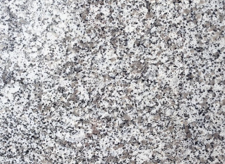 Gros plan d'une surface de granit mouchetée, avec des taches blanches, grises et noires. 
granit st salvy, granit du Tarn 