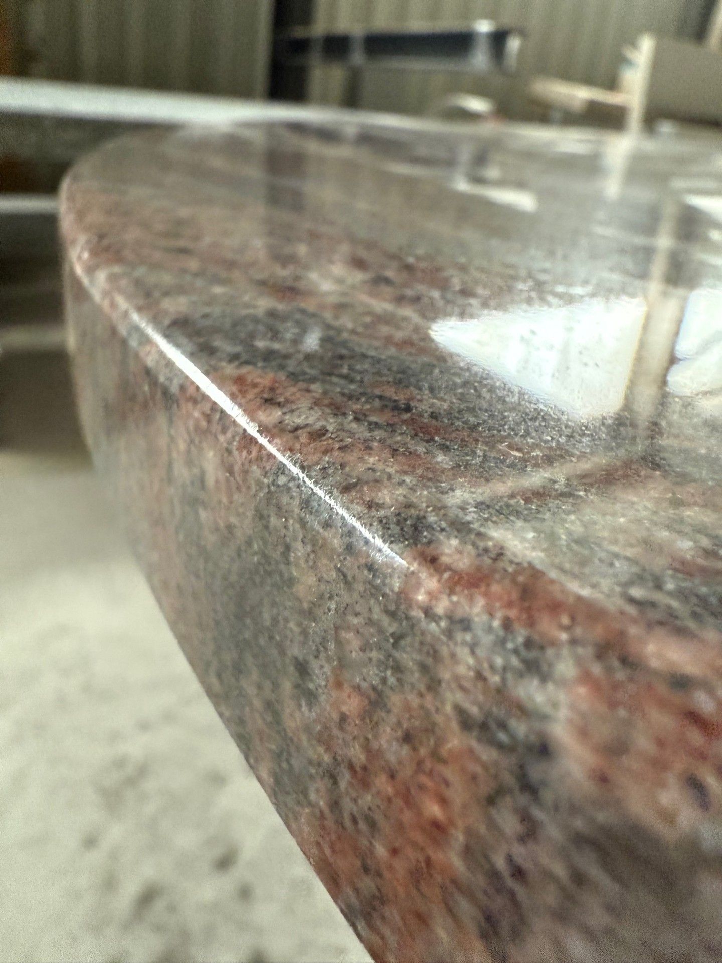 Gros plan d'un comptoir en granit poli avec bord arrondi; nuances de rouge, noir et gris.
