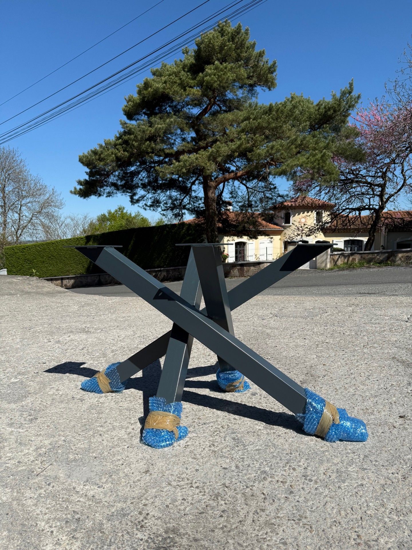 Base de table en métal gris foncé, posée à l'extérieur sur du gravier.