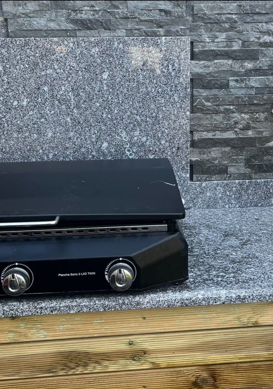 Le barbecue à gaz noir avec boutons est posé sur un comptoir avec un dosseret en pierre.