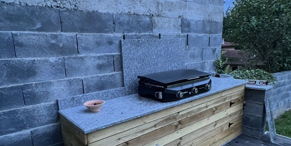 Un gril noir est posé sur un plan de travail, près d'un mur en parpaings. Un petit bol est posé dessus.