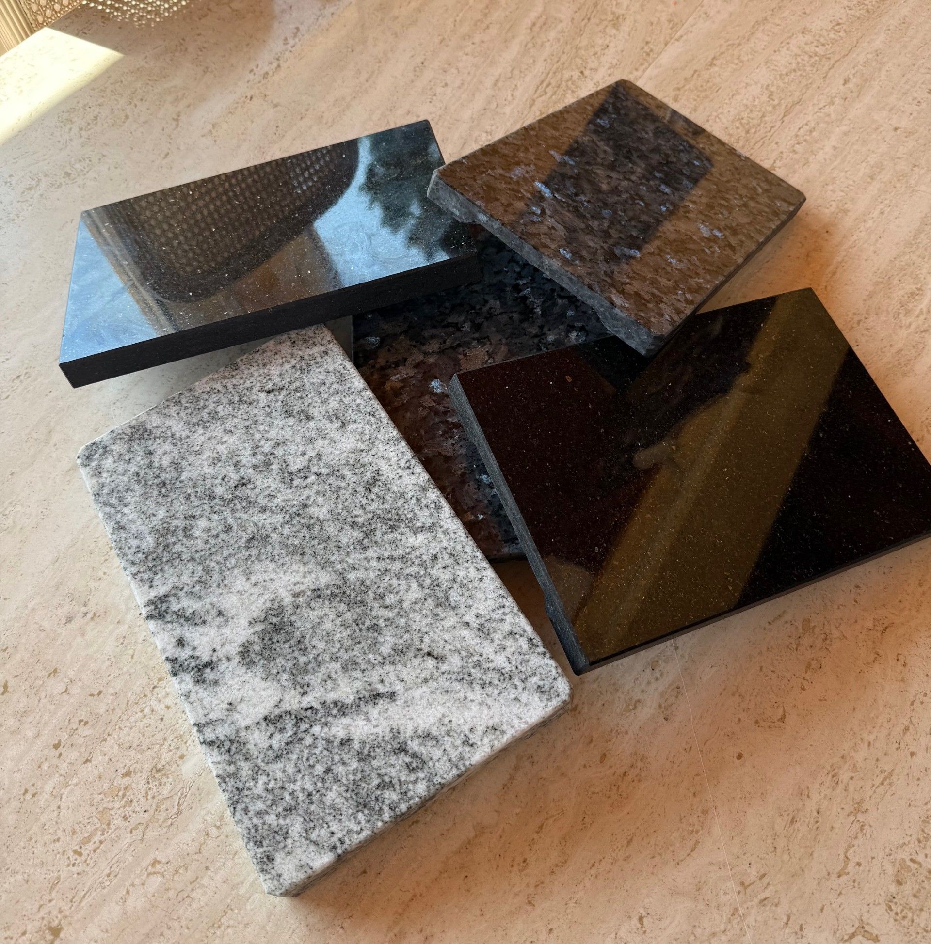 Différents carreaux de granit aux tons de gris, de noir et de blanc moucheté, reposant sur une surface beige.