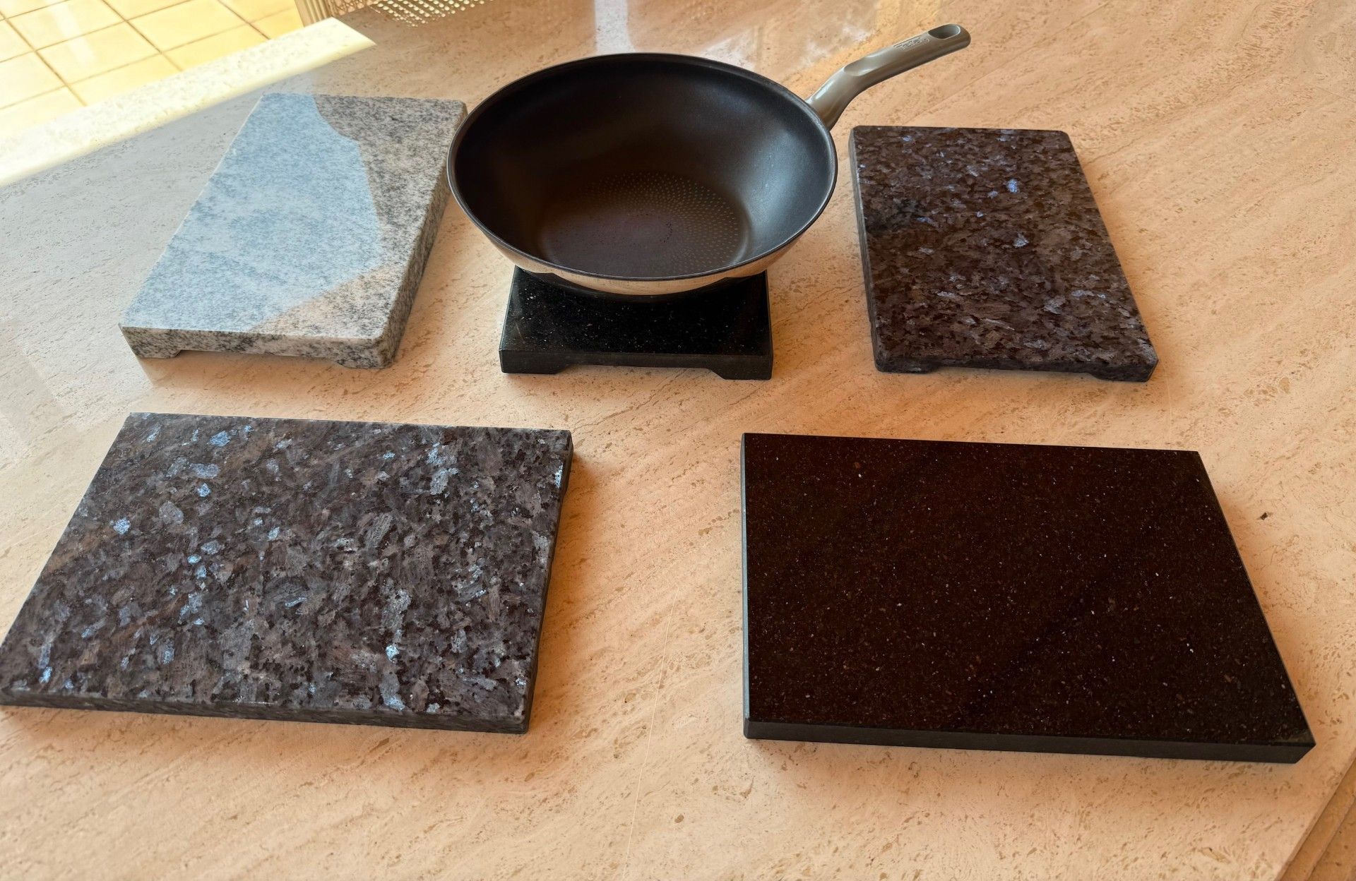 Wok sur pied, entouré d'échantillons de carreaux de granit dans des tons de gris et de marron, sur une surface de couleur claire.