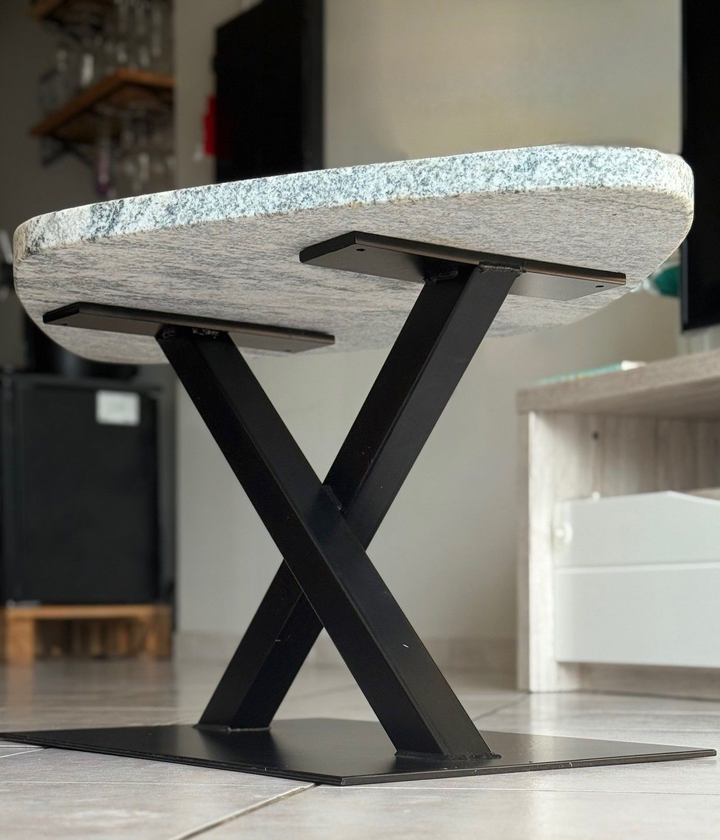 Table basse avec plateau en granit et pieds noirs en forme de X, posée sur une base noire décorative dans un salon.