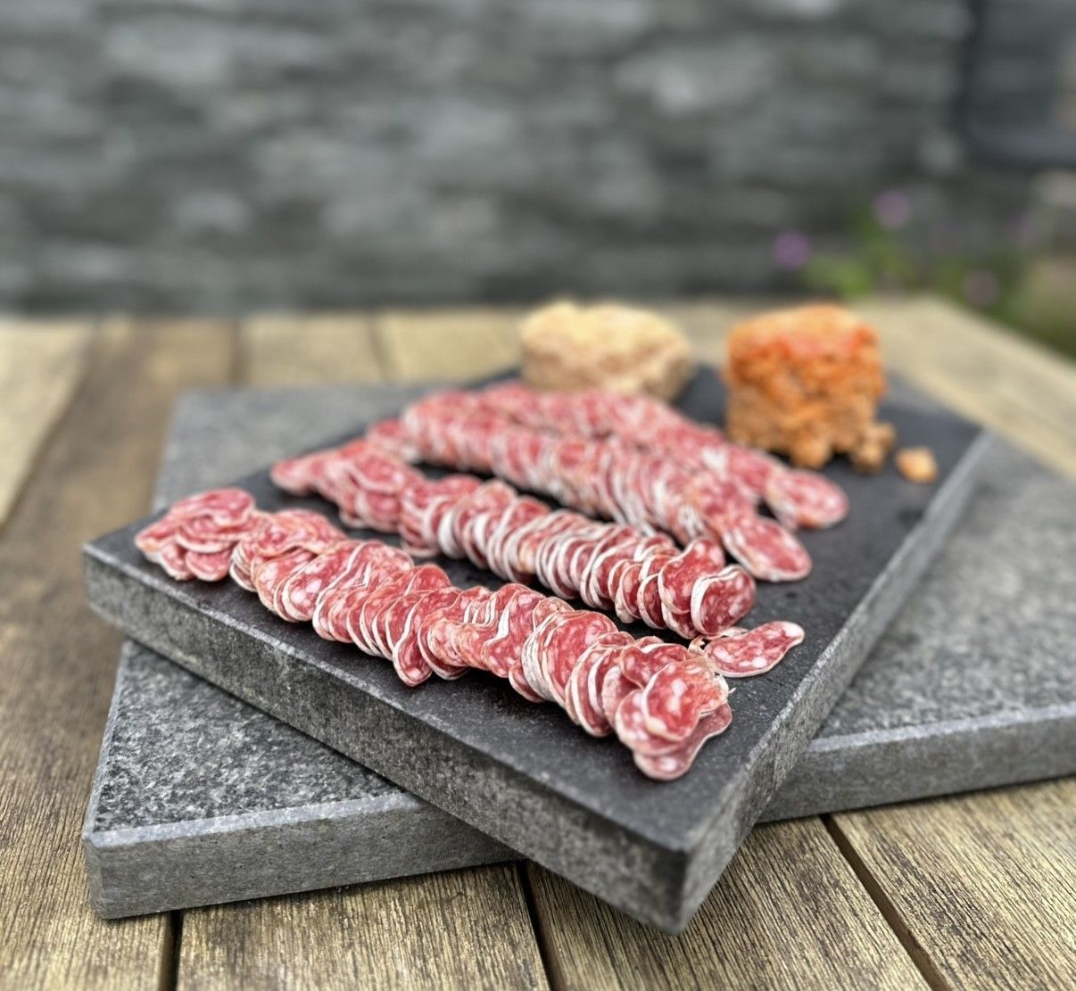 Tranches de saucisse sur une pierre d'ardoise avec de petites portions de nourriture, reposant sur une surface en bois.