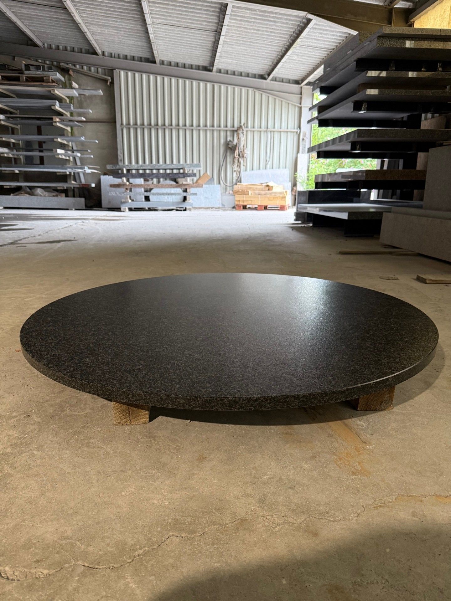 Plateau de table circulaire en granit noir sur supports en bois à l'intérieur d'un entrepôt.
