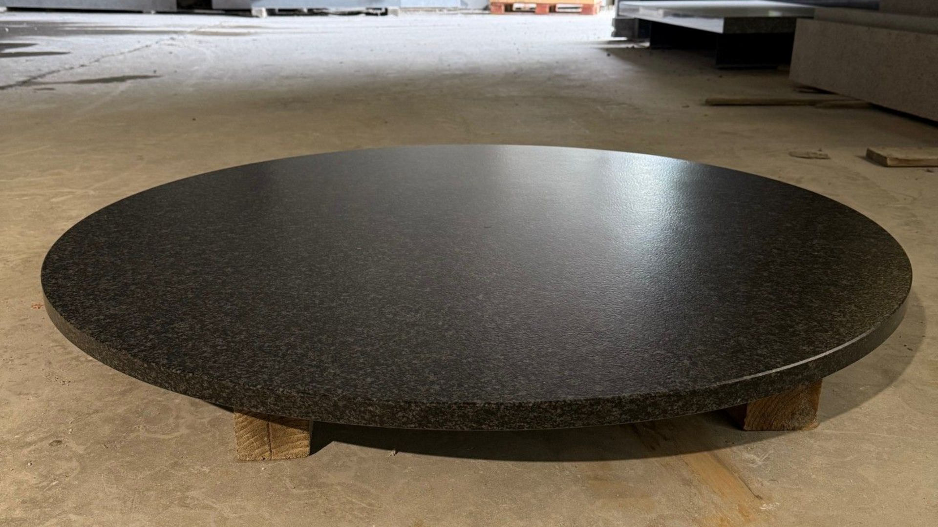 Plateau circulaire en granit noir sur supports en bois.