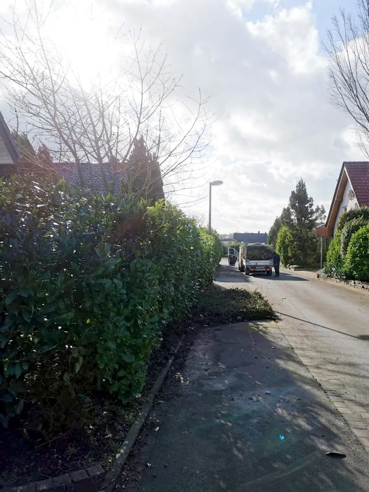 Ein weißer Lieferwagen fährt eine Straße entlang neben einer Hecke