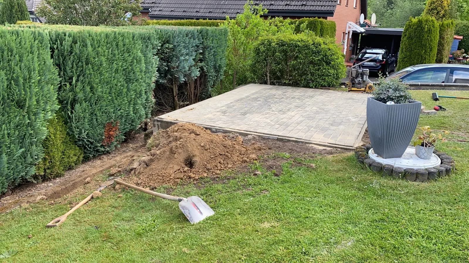 In einem Garten liegt eine Schaufel im Gras neben einer Topfpflanze.