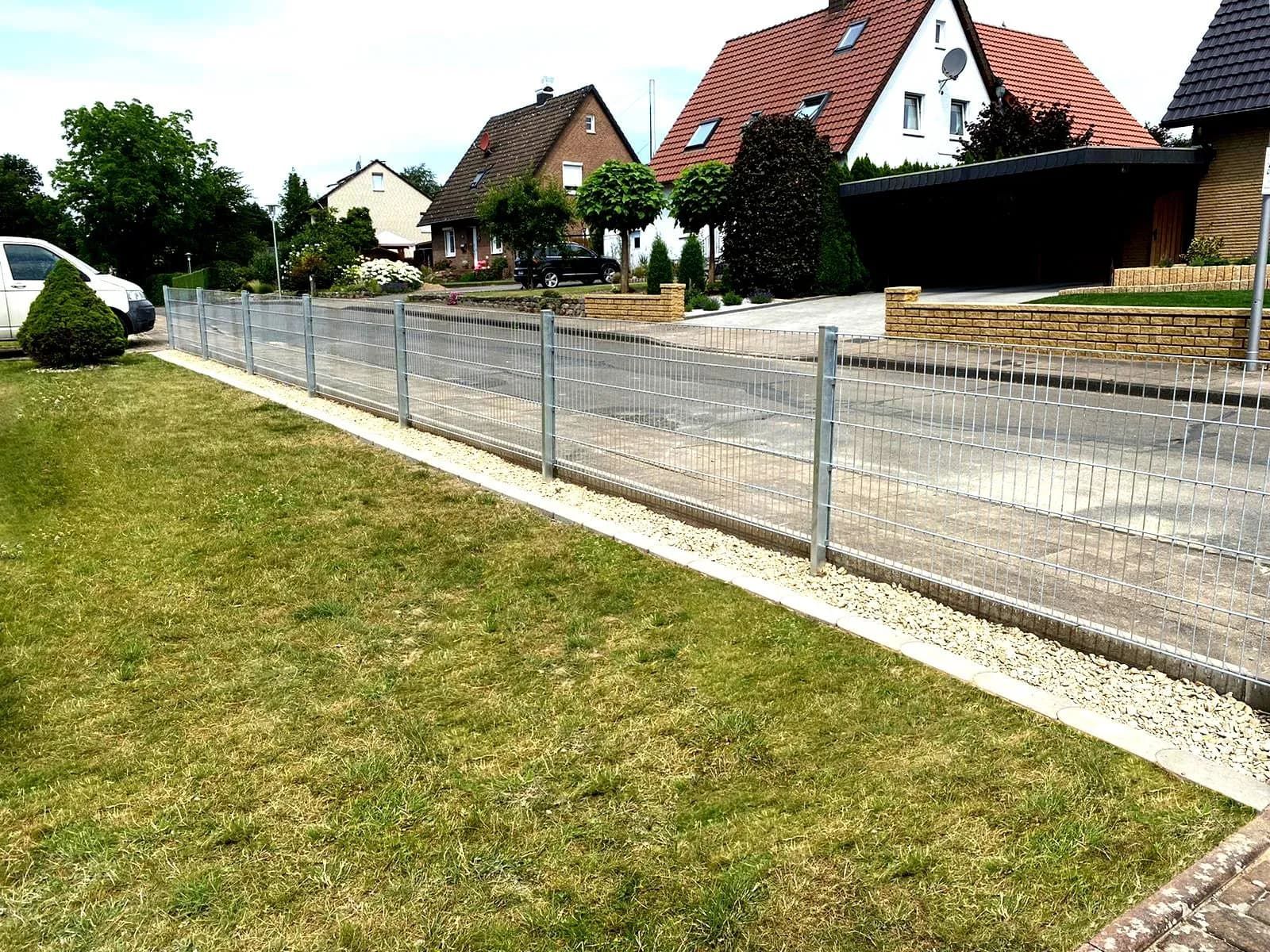 Ein Zaun umgibt einen üppigen grünen Rasen vor einer Häuserreihe.