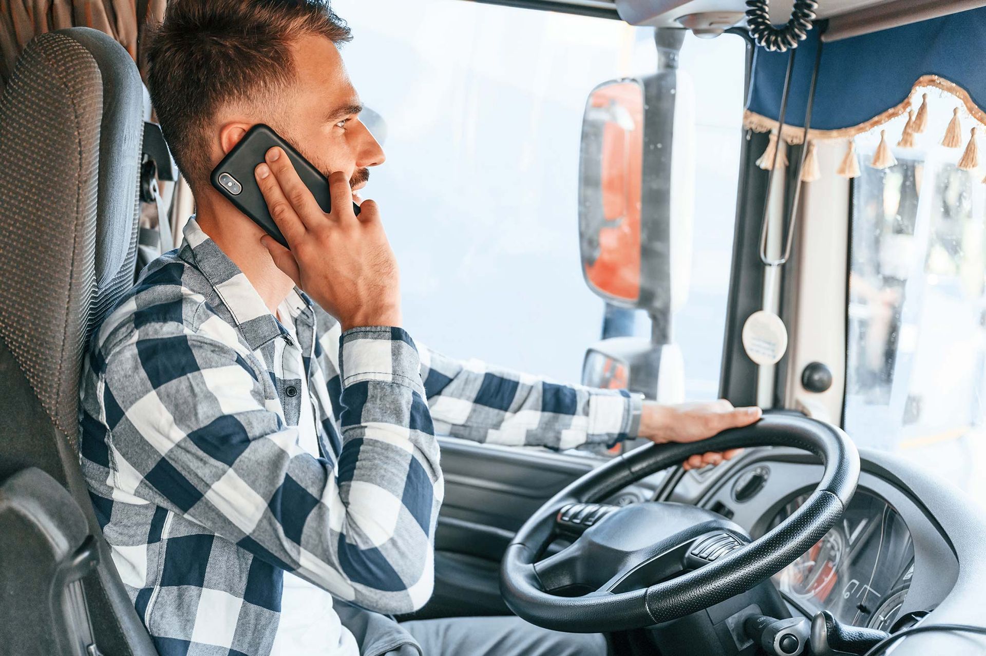 Ein Mann sitzt auf dem Fahrersitz eines Lastwagens und telefoniert mit einem Mobiltelefon.