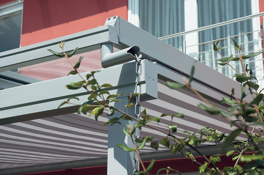 Auf einem Balkon steht eine Pergola mit gestreifter Markise.