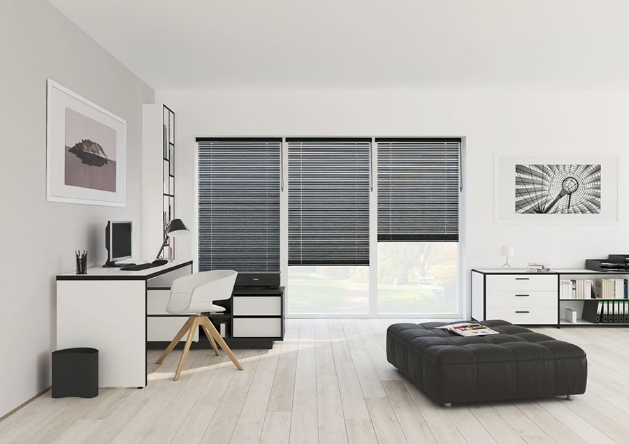 Ein Wohnzimmer mit Schreibtisch, Sessel, Ottomane und Jalousien.