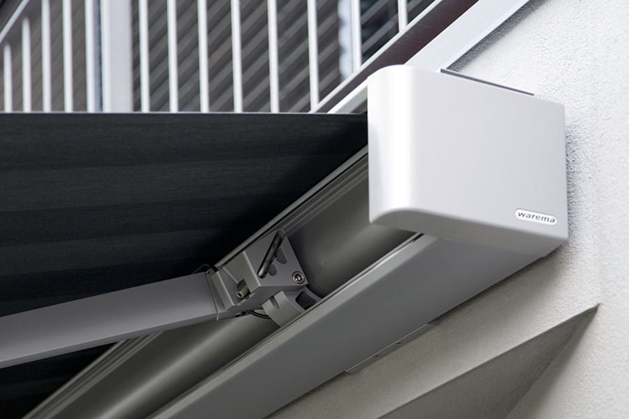 An der Seite eines Gebäudes steht neben einem Balkon ein weißer Kasten.