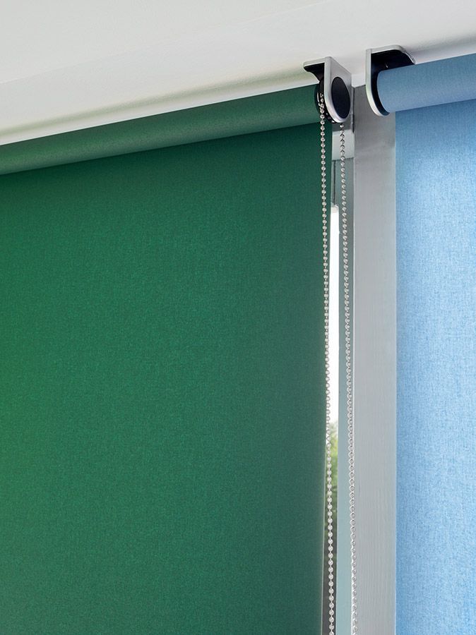 An einem Fenster hängt neben einem blauen Rollo ein grünes Rollo.