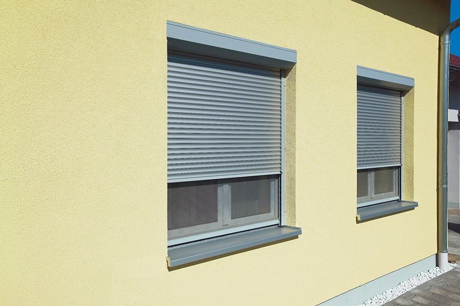 Ein gelbes Gebäude mit zwei Fenstern mit Rollläden.