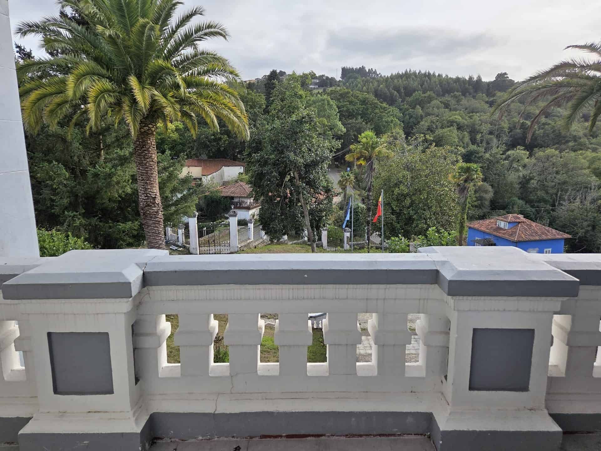 Balcón con balaustrada blanca con vista a un paisaje verde, árboles y edificios.