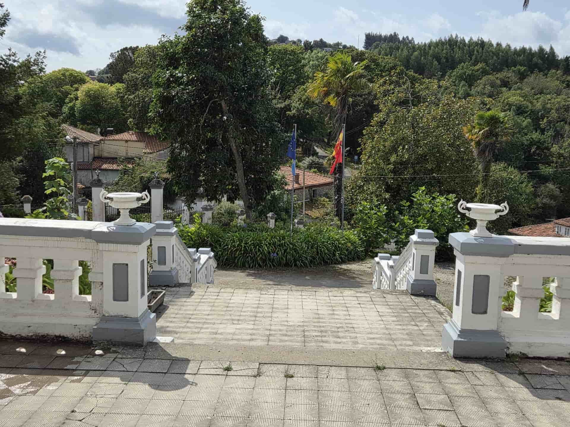 Escalera de piedra que conduce a una exuberante ladera verde con losas; balaustradas blancas y grises flanquean los escalones.