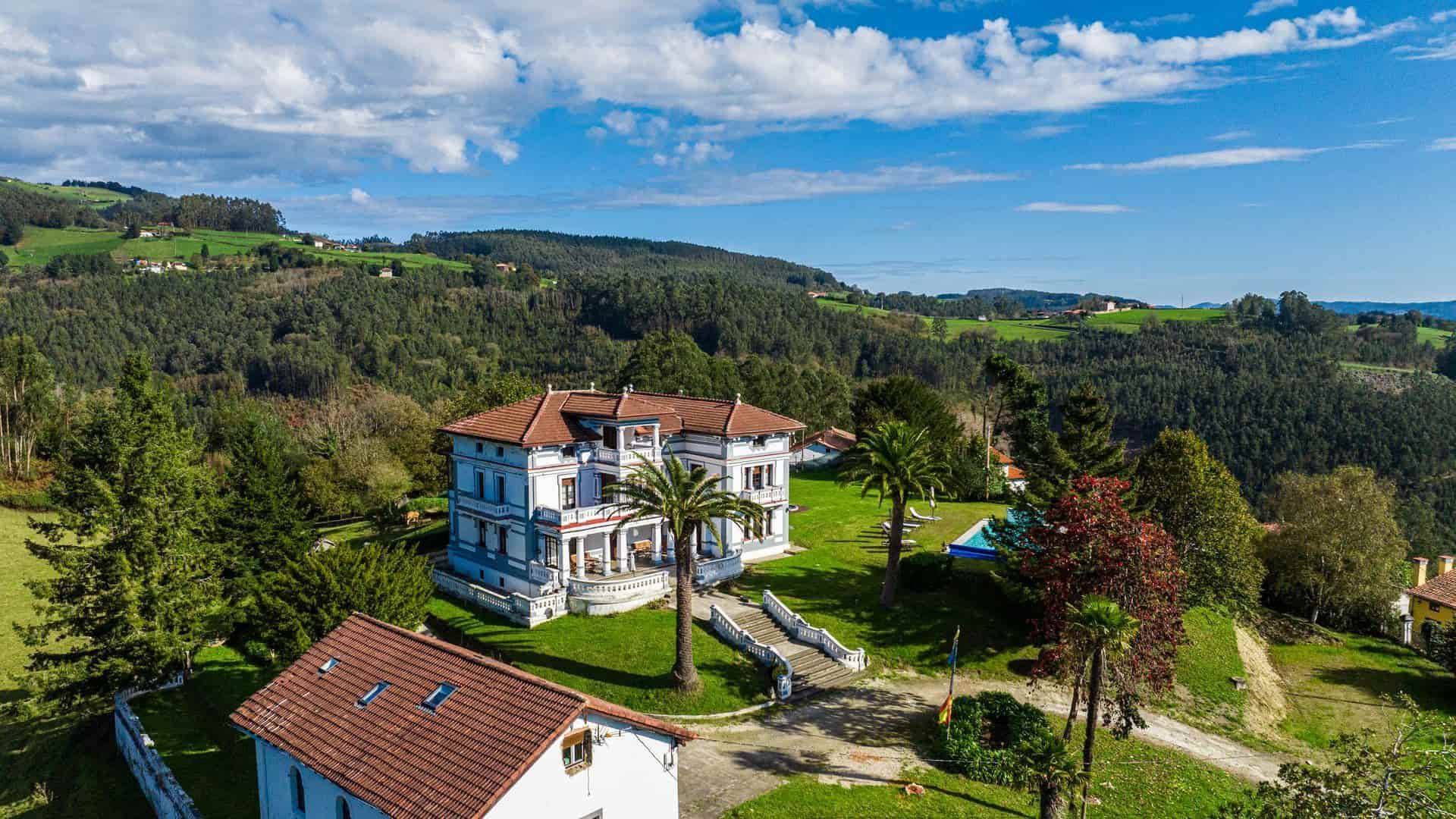 Edificio grande y ornamentado sobre una colina cubierta de hierba, con vistas a un bosque bajo un cielo nublado.