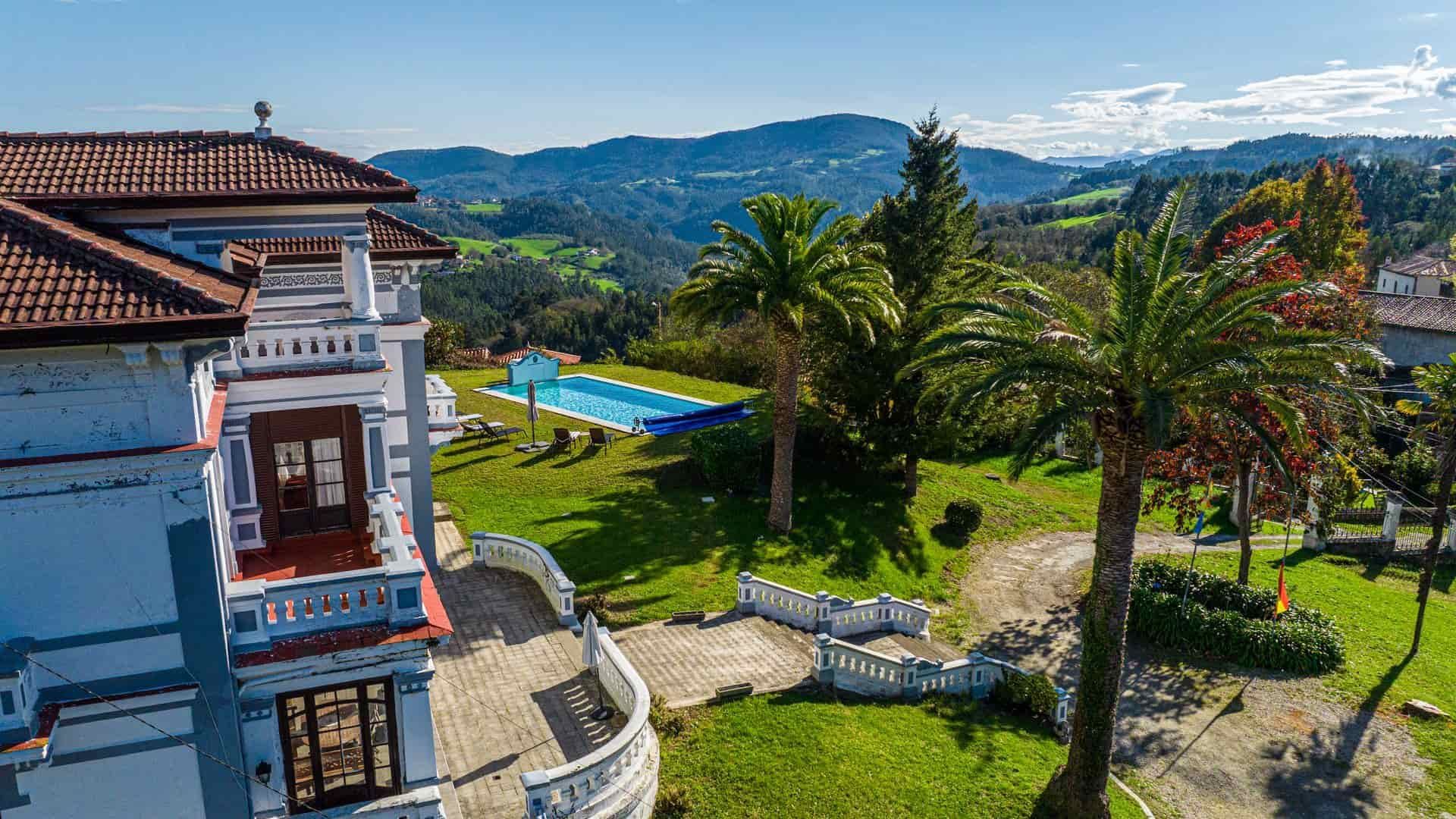 Mansión con piscina, palmeras y fondo de montaña en un día soleado.