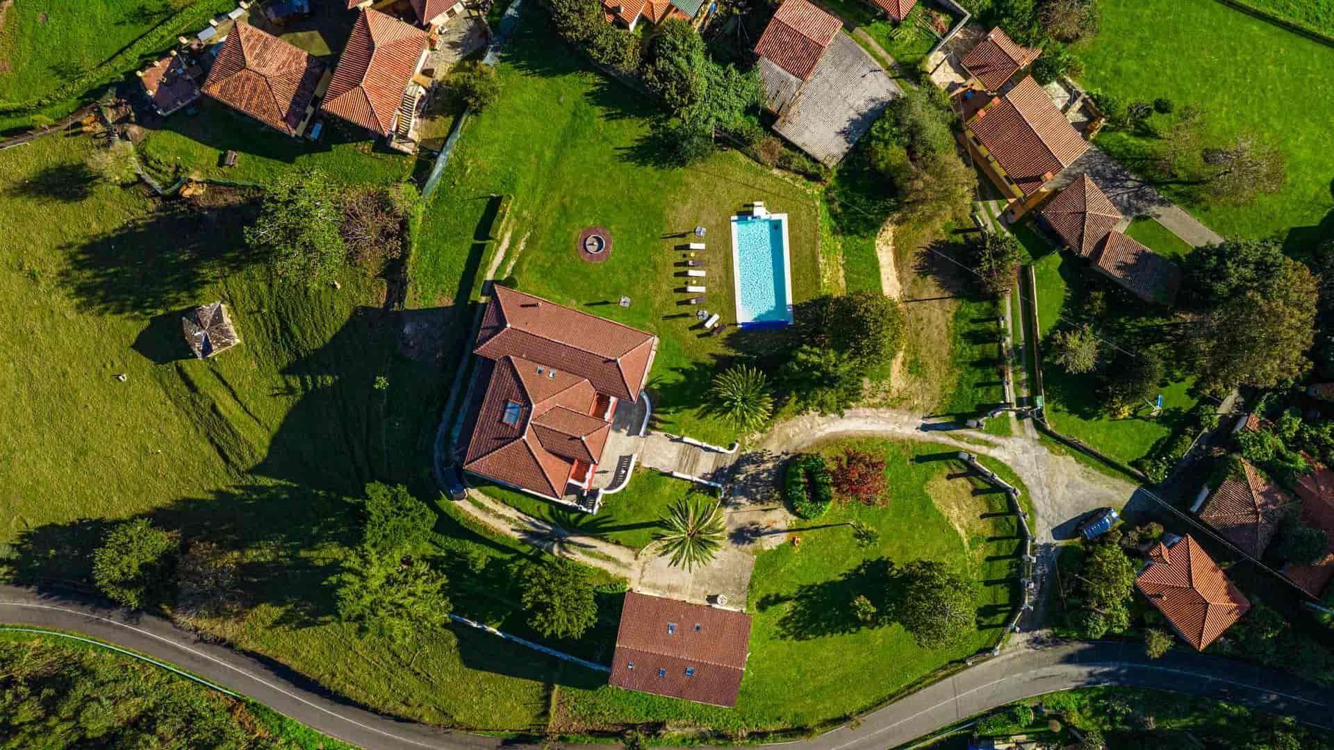 Vista aérea de una casa con piscina rodeada de césped verde y árboles, enclavada en un pequeño pueblo.