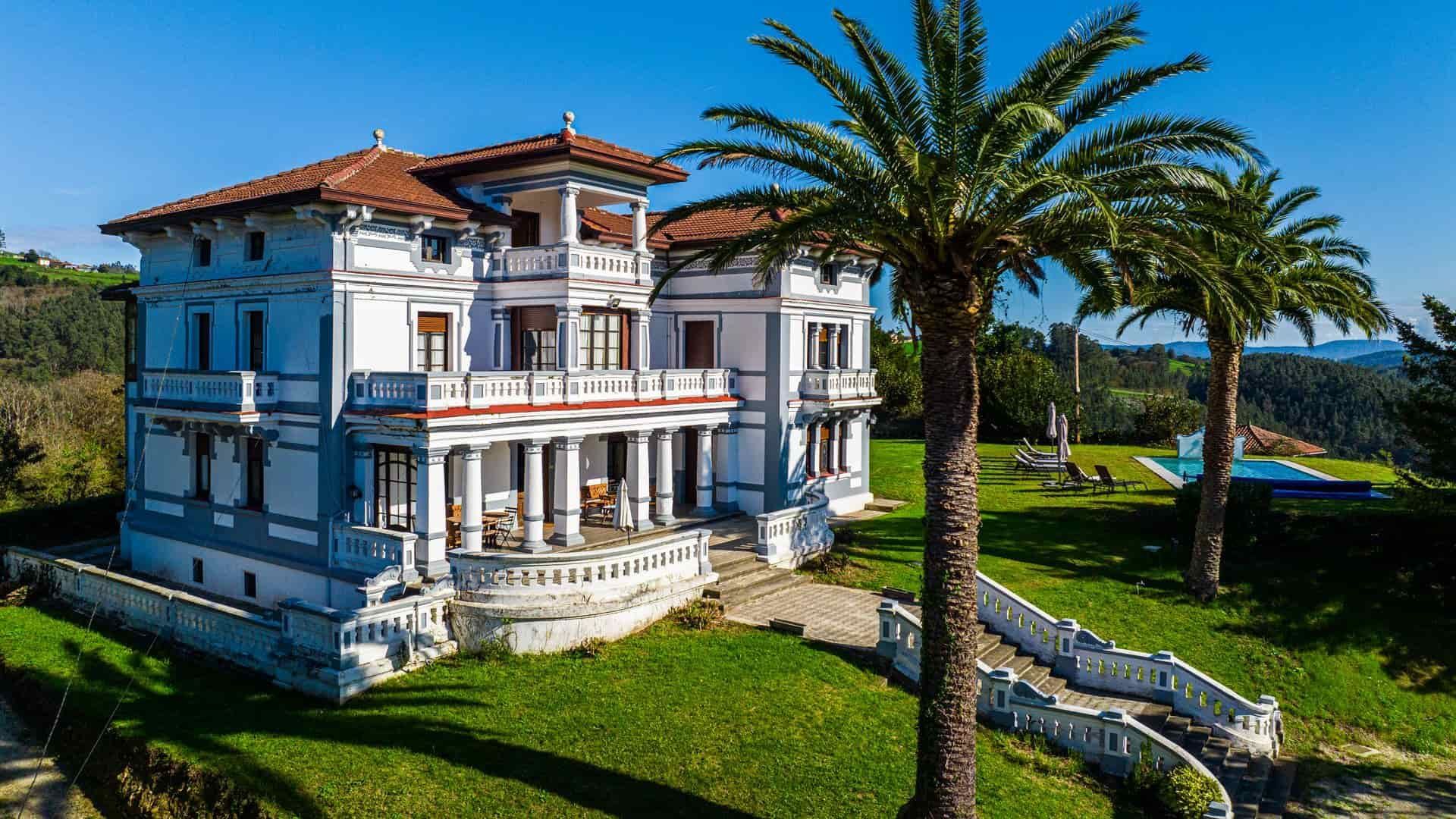 Elegante villa blanca con techo de tejas rojas, palmeras y piscina.