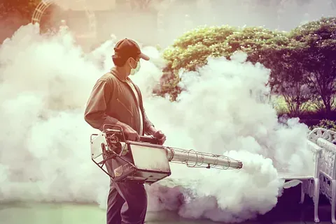Un hombre está usando una máquina para rociar humo en un parque.