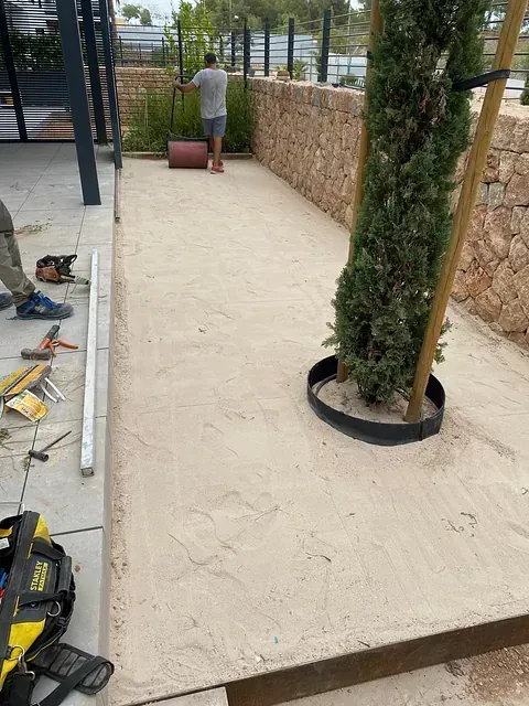 Un hombre está trabajando en un patio con un árbol al fondo.