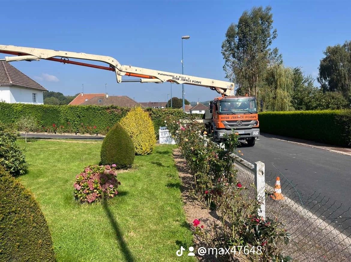 Une mini-pelle orange et blanche creuse une tranchée dans la terre à côté d'un bâtiment en construction.