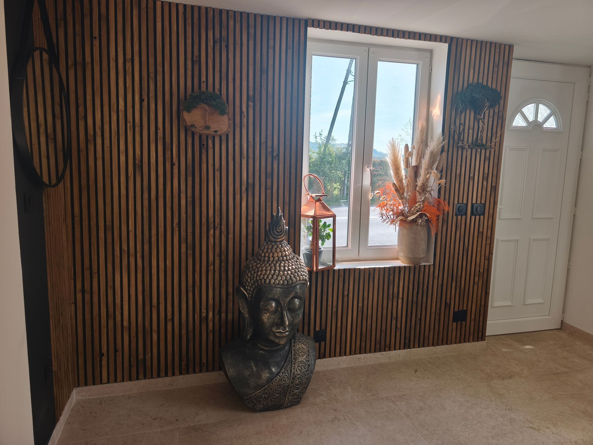 Un bureau mansardé avec parquet blanc, un bureau et une chaise, un fauteuil en osier et un mur en bois sous une lucarne inclinée.