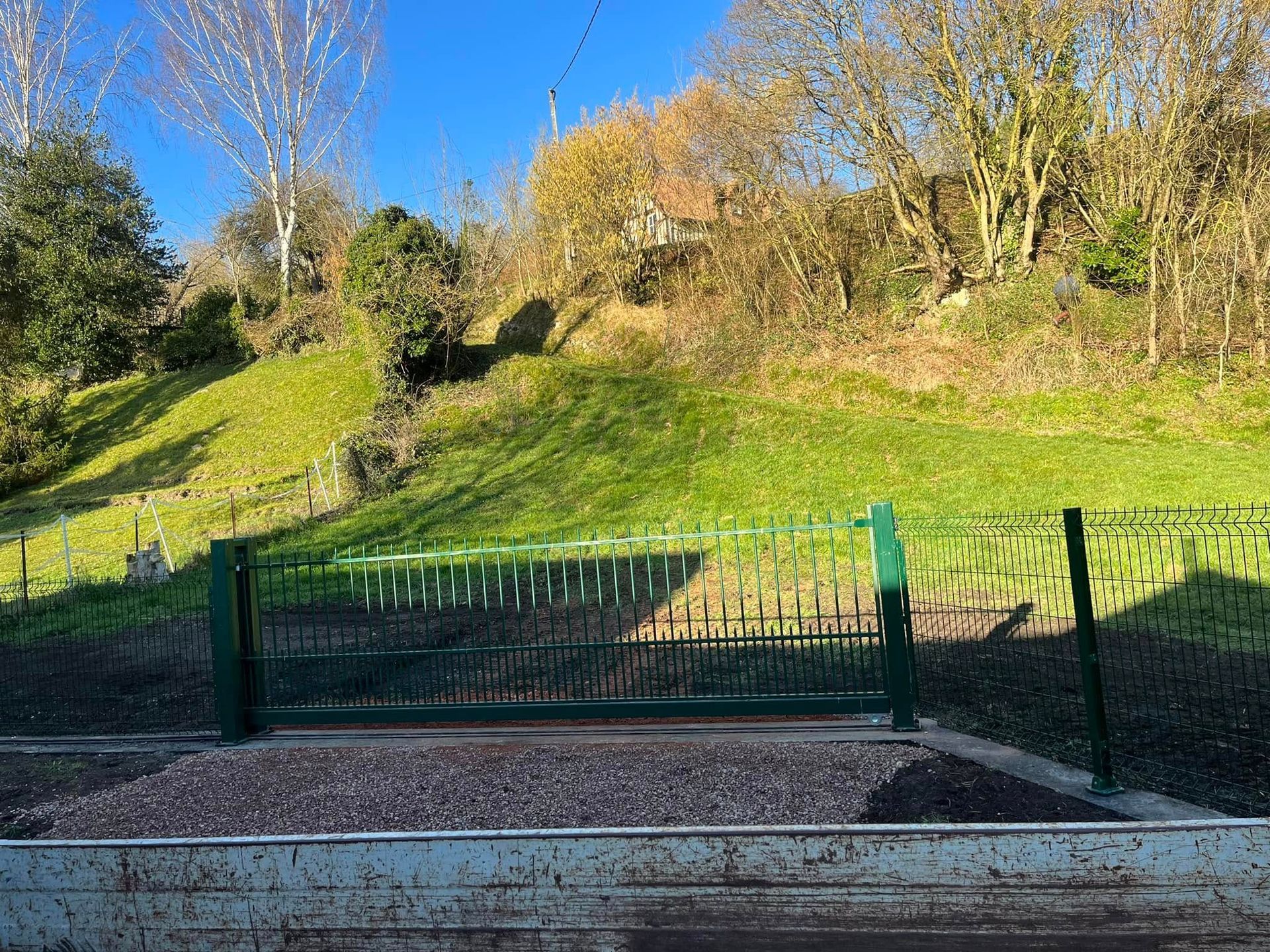 Une clôture métallique gris foncé à double barreaux se dresse devant un jardin résidentiel verdoyant et une maison.