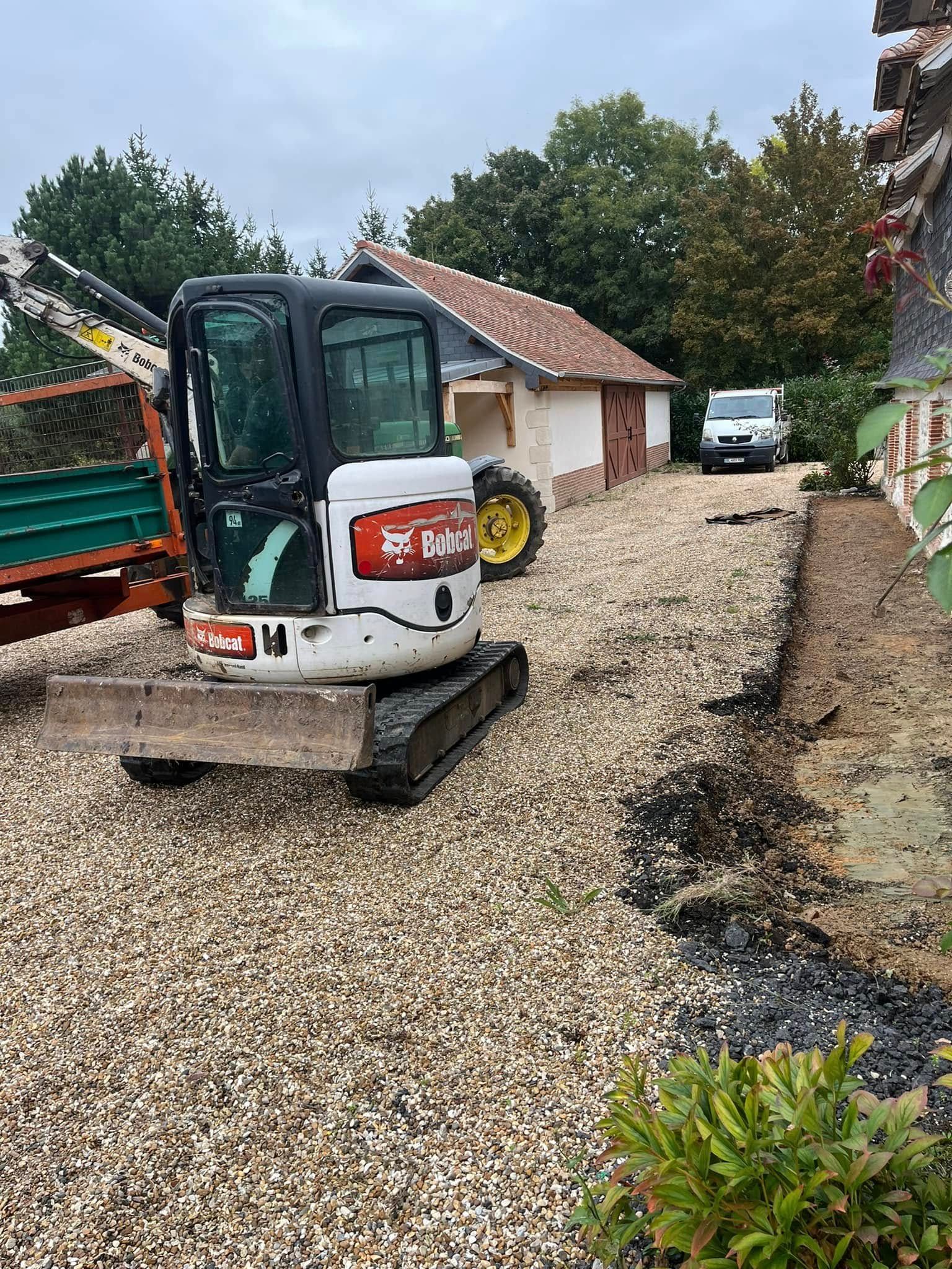 Une mini-pelle orange et blanche creuse une tranchée dans la terre à côté d'un bâtiment en construction.
