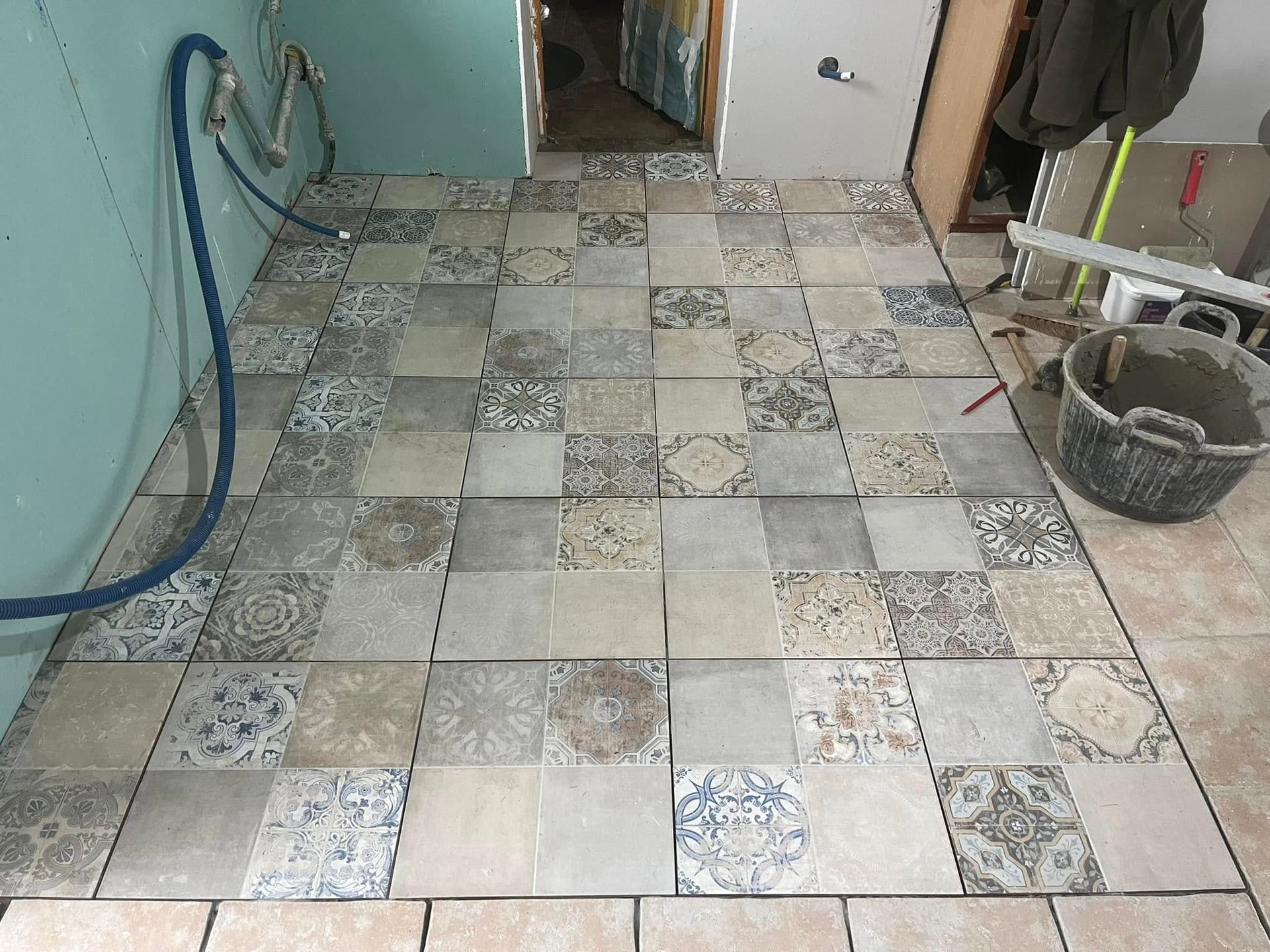 Une personne agenouillée sur un sol en béton, en train d'installer des lames de parquet stratifié imitation bois, un marteau à proximité.