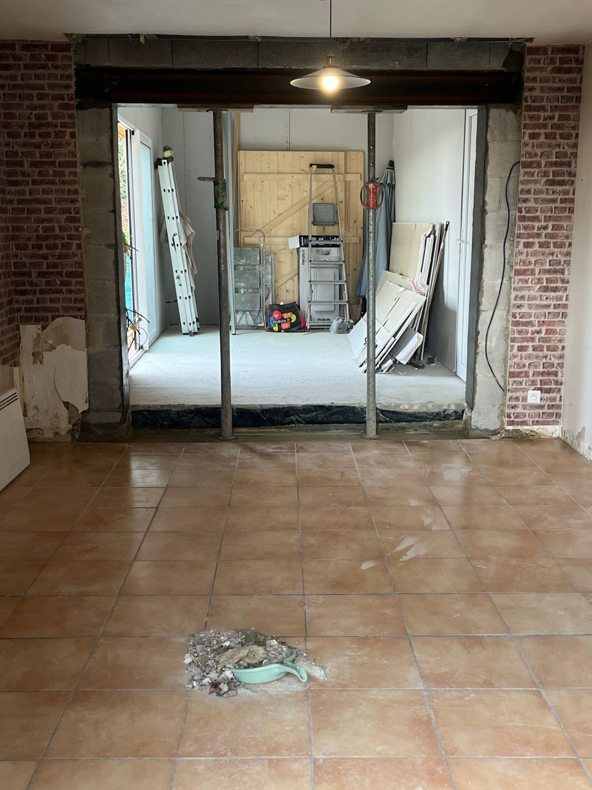 Un chantier de construction montrant des murs en parpaings de béton gris, des portes intérieures, des câbles électriques apparents et des outils sur un sol en béton.